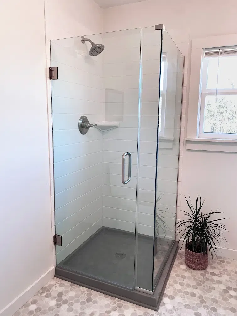Corner glass shower with white subway-look solid-surface walls and gray base